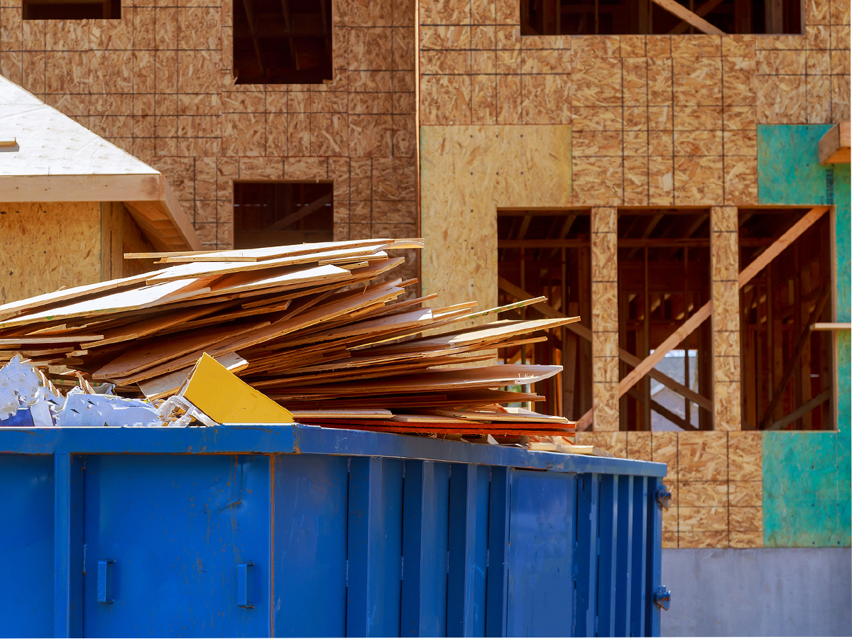 Dumpster holding construction materials in front of a new build